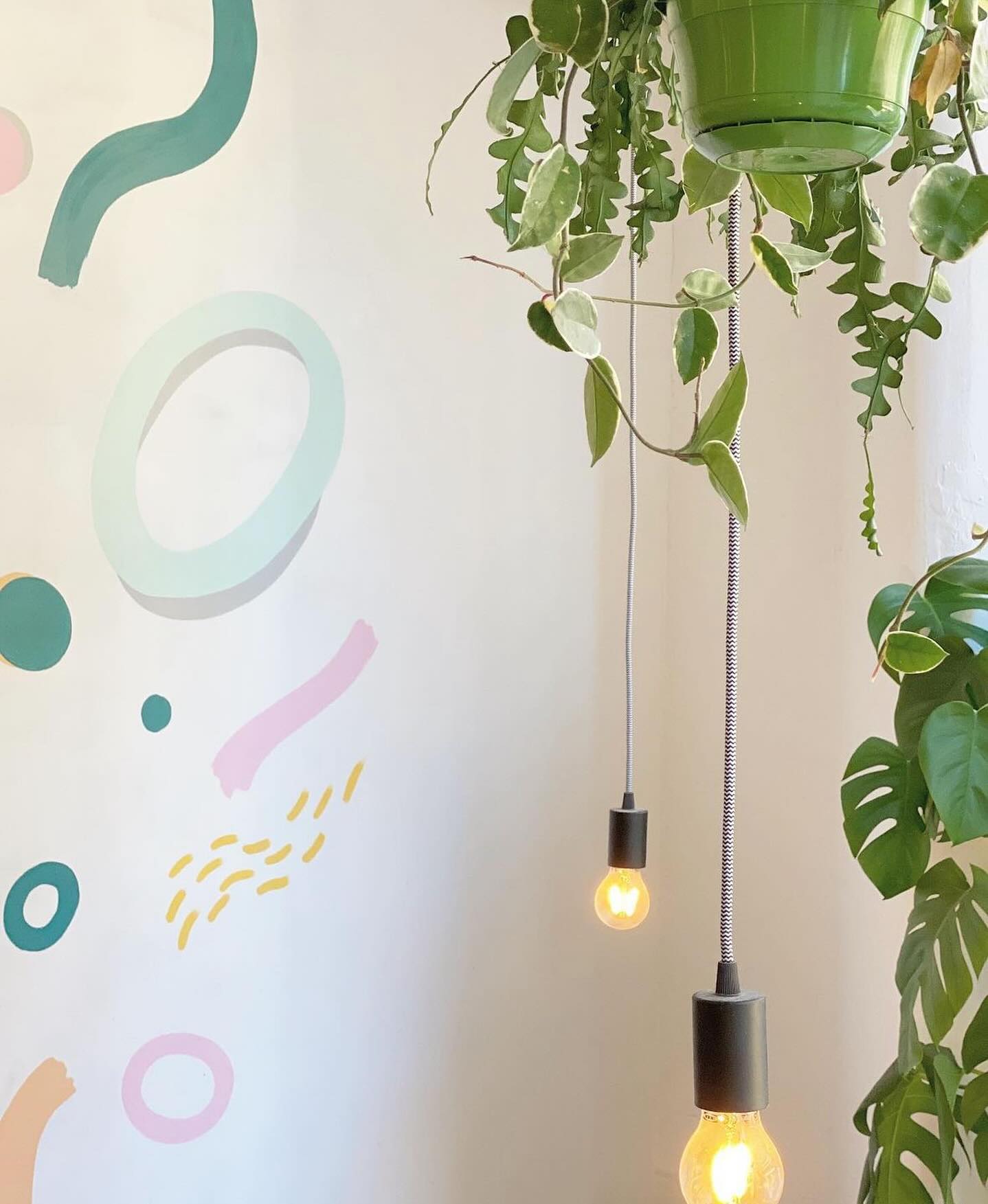 Trailing plants and bare-bulb pendants beside the pastel mural inside Idle Hands